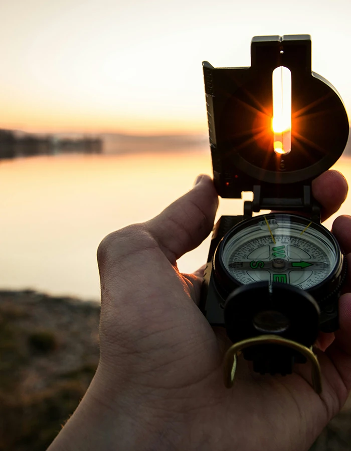 A hand holding a compass at sunset